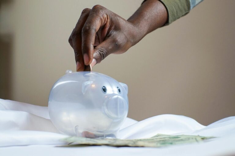 Emergency Fund Secure: Unexpected Costs Vanish, Peace Realized Close-up of a person's hand placing coins into a transparent piggy bank to save money.